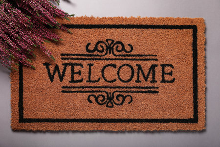 Doormat with word Welcome and heather flowers on gray background, flat layの写真素材