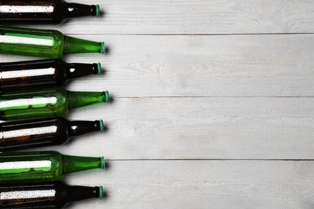 Glass bottles of beer on gray wooden background, flat lay. Space for textの写真素材