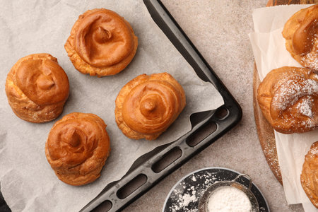 Delicious profiteroles with powdered sugar on gray table, flat lay