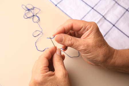 Closeup view of woman threading needle at beige table
