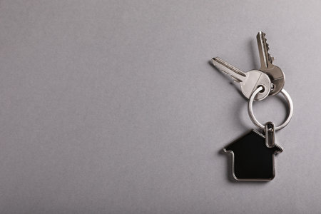 Keys with trinket in shape of house on gray background, top view and space for text. real estate agent servicesの写真素材