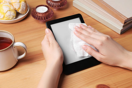 Woman wiping smartphone with paper at wooden table, closeupの写真素材