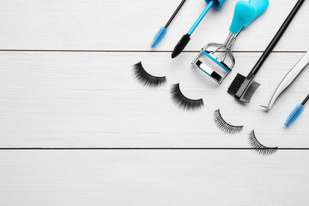 Flat lay composition with false eyelashes and tools on white wooden table. Space for text