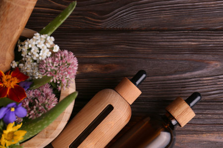 Glass bottles of aromatic essential oil and mortar with different herbs on wooden table, flat lay. Space for textの写真素材