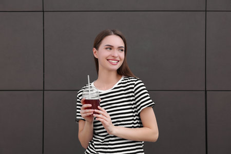 Young woman with plastic cup of fresh juice near brown wallの写真素材