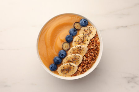 Delicious smoothie bowl with fresh blueberries, banana and granola on white marble table, top viewの写真素材