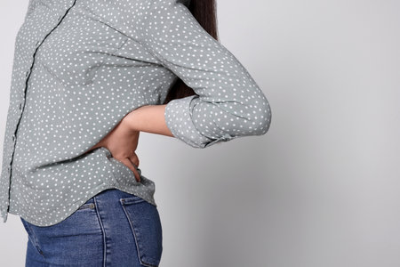 Young woman suffering from pain in back on light gray background, closeup with space for text. arthritis symptomsの写真素材