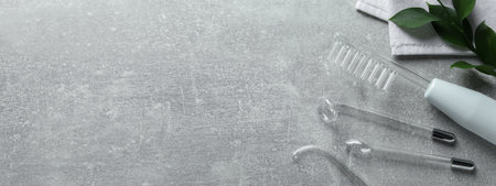 High frequency darsonval device, different nozzles, leaves and towel on gray background, flat lay. Banner design with space for textの写真素材