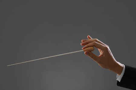 Professional conductor with baton on gray background, closeup. Space for text