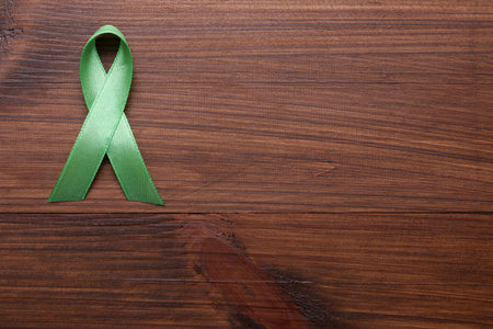 World Mental Health Day. Green ribbon on wooden background, top view with space for textの写真素材