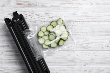 Vacuum packing sealer with plastic bag of cucumbers on white wooden table, flat lay. Space for textの写真素材