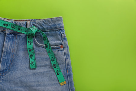 Jeans and measuring tape on light green background, top view with space for text. weight loss conceptの写真素材