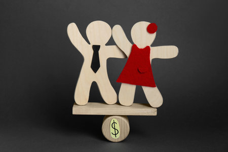 gender pay gap. Wooden figures of man and woman on miniature seesaw against black backgroundの写真素材
