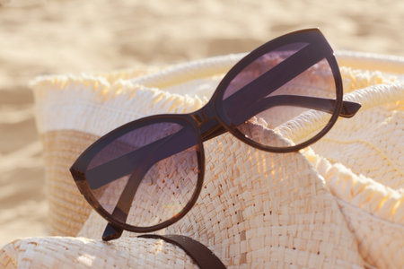 Hat and bag with beautiful sunglasses on sandy beach, closeup