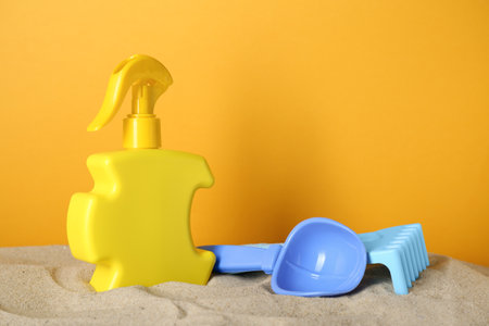 Suntan product and plastic beach toys on sand against yellow backgroundの写真素材