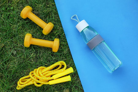 Skipping rope, dumbbells, fitness mat and bottle of water on green grass, flat lay. morning exerciseの写真素材