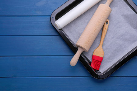 Baking parchment papers, rolling pin and brush on blue wooden table, flat lay. Space for textの写真素材
