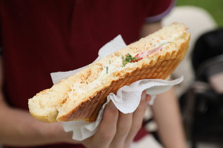 Man holding delicious sandwich outdoors, closeup. street food