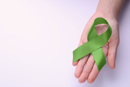 World Mental Health Day. Woman holding green ribbon on white background, top view with space for textの写真素材