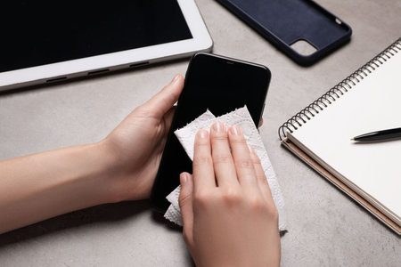 Woman wiping smartphone with paper towel at gray table, closeupの写真素材