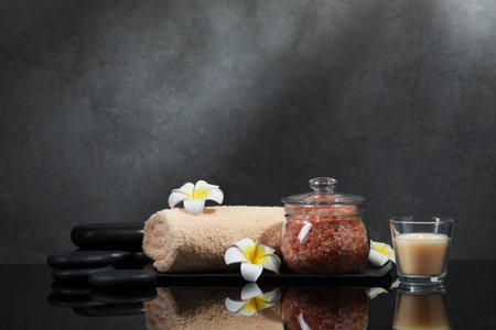 Glass jar with natural sea salt, beautiful flowers, candle and spa stones on mirror surfaceの写真素材