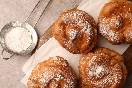 Delicious profiteroles with powdered sugar on gray table, flat lay