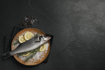 Sea bass fish and ingredients on black table, flat lay. Space for textの写真素材