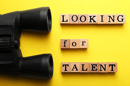 staff recruitment concept. Phrase Looking For Talent made of wooden cubes and binoculars on yellow background, flat layの写真素材