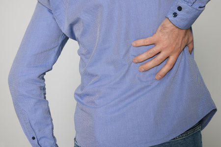 Man suffering from pain in back on light background, closeup. arthritis symptomsの写真素材