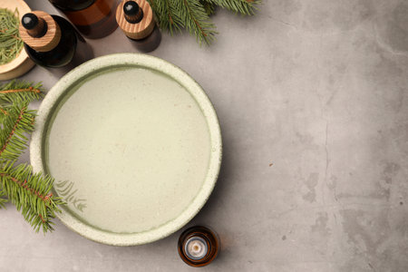 Bowl of essential oil and fir twigs on gray table, flat lay with space for text. Aromatherapy treatmentsの写真素材