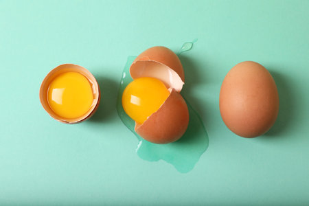 Cracked and whole chicken eggs on turquoise background, flat layの写真素材