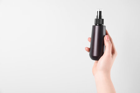 Woman holding spray bottle with hair thermal protection on white background, closeup. Space for textの写真素材