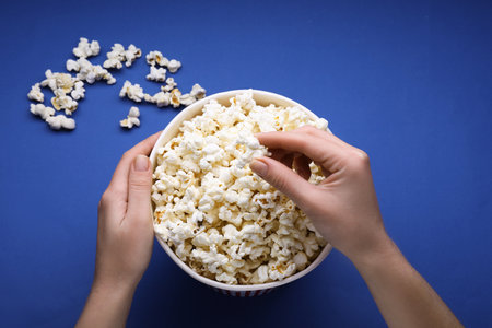Woman taking fresh popcorn from bucket on blue background, above viewの写真素材
