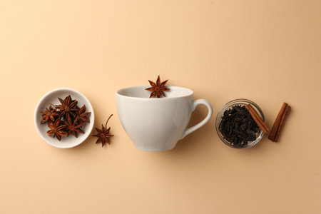 Cup with anise stars, dry tea and cinnamon sticks on beige background, flat layの写真素材