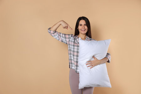 Happy young woman pointing at soft pillow on beige background, space for textの写真素材