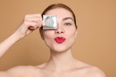 Woman holding condom on beige background. safe sexの写真素材