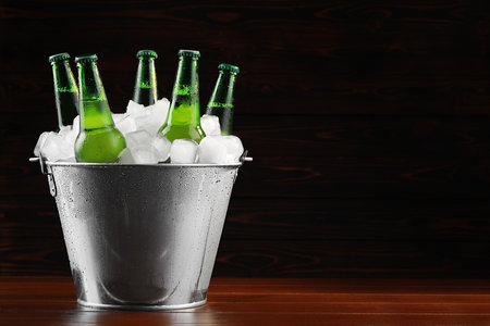 Metal bucket with bottles of beer and ice cubes on wooden background, space for textの写真素材