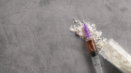 Plastic container of powder and syringe on gray table, flat lay with space for text. hard drugs