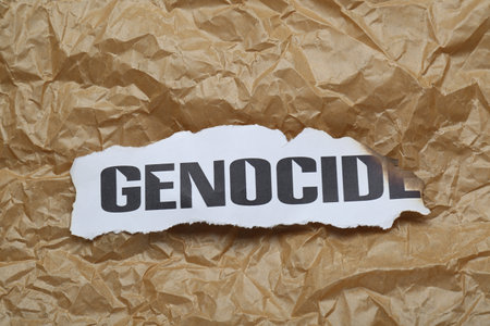 Piece of burnt card with word Genocide on crumpled paper, top viewの写真素材