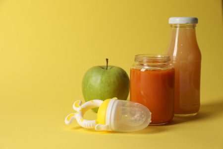 Healthy baby food, apple, juice and nibbler on yellow background, space for textの写真素材