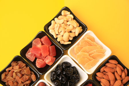 Bowls with dried fruits and nuts on yellow background, flat layの写真素材