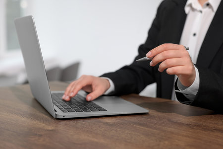 Woman with pen working on laptop at wooden table, closeup. Electronic document managementの写真素材