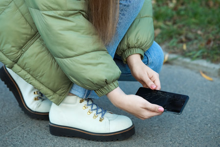 Woman taking dropped smartphone from asphalt outdoors, closeup. device repairの写真素材