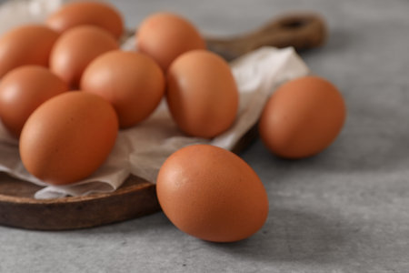 Chicken eggs, wooden board and parchment paper on gray table, closeup