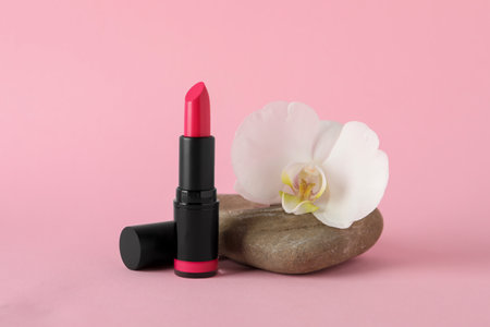 Beautiful lipstick and orchid flower on stone against pink backgroundの写真素材