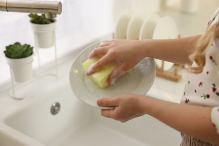 Little girl washing plate above sink, closeupの写真素材