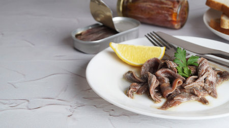 Plate with canned anchovy fillets and lemon wedge on white textured table, closeup. Space for textの写真素材