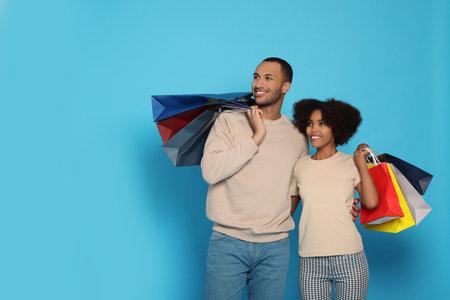 Happy African American couple with shopping bags on light blue background. Space for textの写真素材