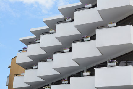 Exterior of building with balconies decorated with beautiful flowers against blue sky, low angle viewのeditorial素材