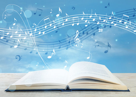 Music flow from book. Musical symbols flying over tome on white wooden table against skyの写真素材